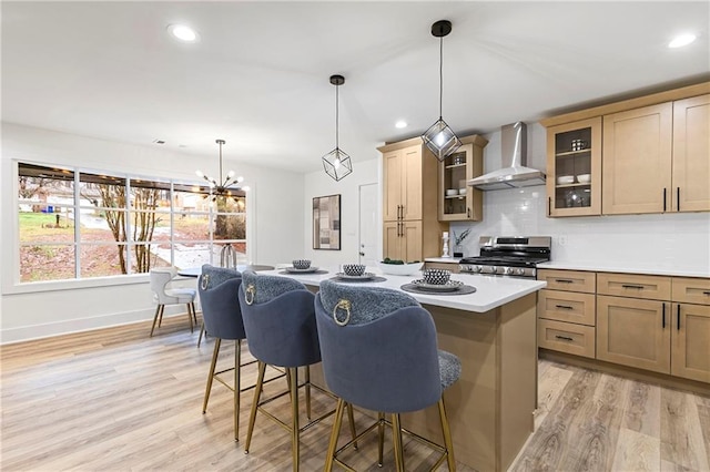 kitchen featuring a center island, wall chimney range hood, a breakfast bar area, stainless steel range oven, and light wood-style flooring