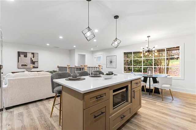 kitchen with stainless steel microwave, a kitchen island, open floor plan, light wood-type flooring, and a kitchen bar