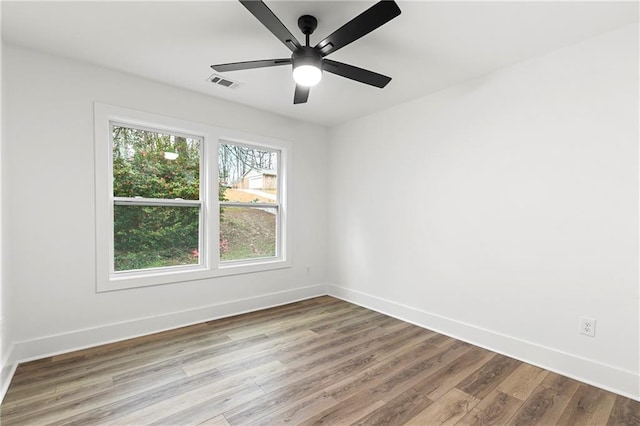 spare room with wood finished floors, visible vents, and baseboards