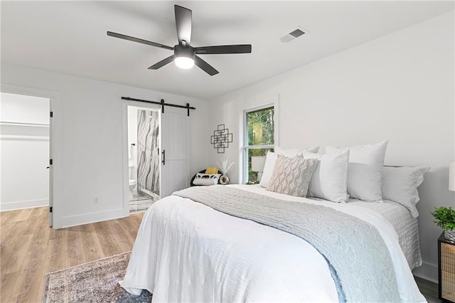 bedroom with visible vents, a walk in closet, baseboards, a barn door, and light wood-style floors