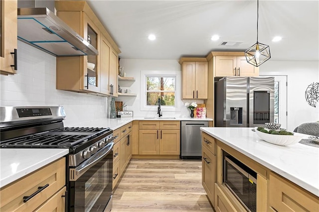 kitchen featuring light brown cabinetry, stainless steel appliances, wall chimney exhaust hood, and a sink