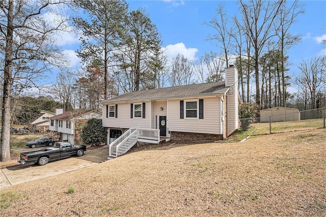 raised ranch with a front yard, concrete driveway, fence, and a chimney