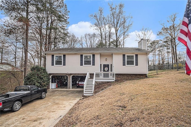 bi-level home featuring a front lawn, driveway, fence, a carport, and a chimney