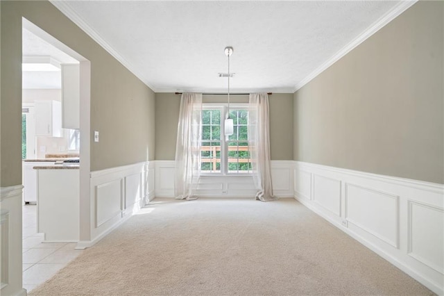 unfurnished dining area with a decorative wall, wainscoting, light colored carpet, and crown molding