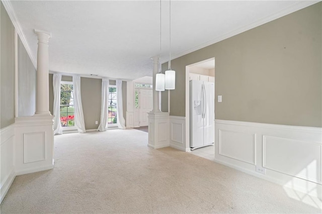 spare room with decorative columns, light colored carpet, a decorative wall, crown molding, and a wainscoted wall