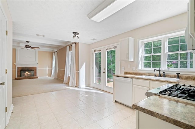kitchen with dishwasher, a sink, ceiling fan, french doors, and a fireplace