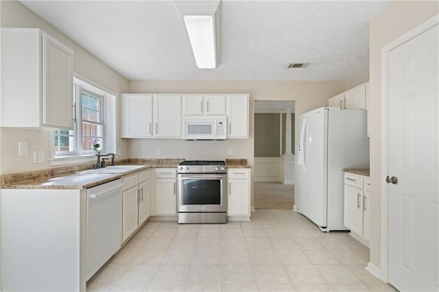 kitchen with white appliances, a sink, white cabinetry, and light countertops