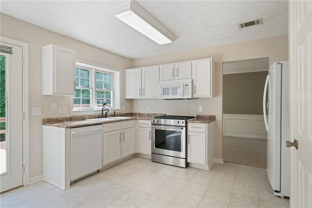 kitchen featuring white appliances, a sink, white cabinets, and light carpet