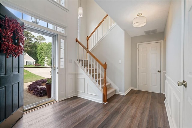 foyer featuring dark wood finished floors, stairway, healthy amount of natural light, wainscoting, and a decorative wall