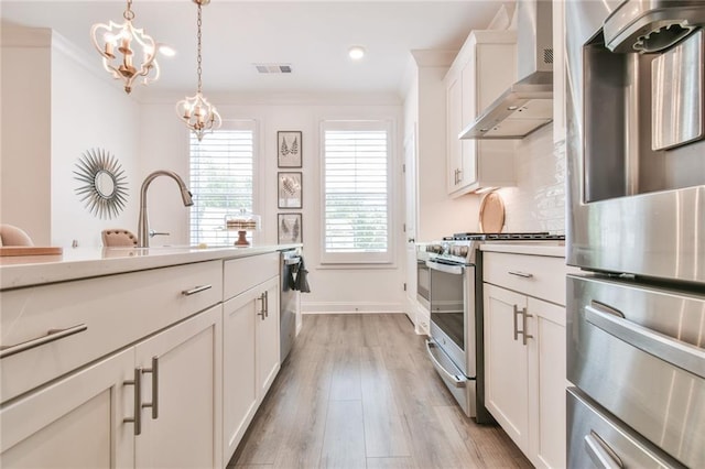 kitchen with a sink, stainless steel appliances, visible vents, wall chimney exhaust hood, and an inviting chandelier