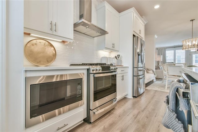 kitchen with light wood-style flooring, white cabinets, wall chimney range hood, appliances with stainless steel finishes, and tasteful backsplash