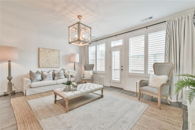 living area with baseboards, an inviting chandelier, visible vents, and wood finished floors