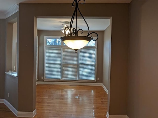 unfurnished dining area with a chandelier, ornamental molding, wood finished floors, and baseboards