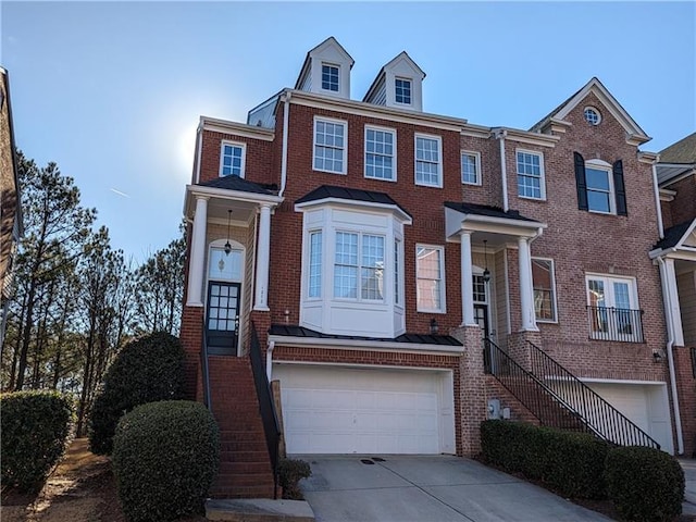 multi unit property with driveway, brick siding, stairway, and an attached garage