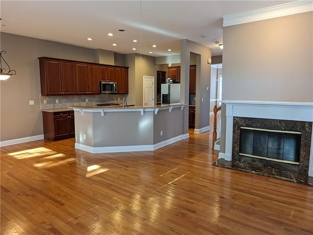 kitchen featuring decorative backsplash, appliances with stainless steel finishes, light countertops, light wood-style floors, and a kitchen bar