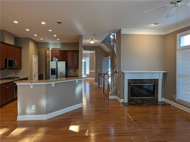 kitchen featuring ceiling fan, a kitchen breakfast bar, wood finished floors, stainless steel appliances, and a high end fireplace