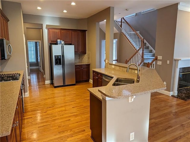 kitchen with light wood-style floors, a fireplace, stainless steel appliances, and a sink