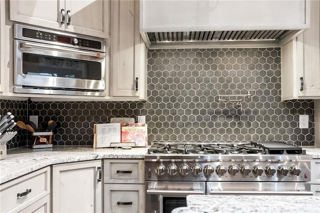 kitchen with appliances with stainless steel finishes, tasteful backsplash, light stone counters, and wall chimney range hood