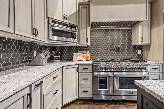 kitchen with premium range hood, decorative backsplash, light stone counters, and appliances with stainless steel finishes