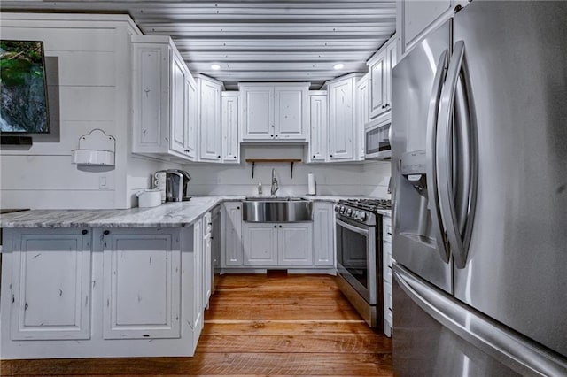 kitchen with sink, appliances with stainless steel finishes, light hardwood / wood-style floors, light stone counters, and white cabinetry