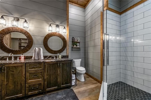 bathroom featuring a tile shower, vanity, toilet, and wooden walls