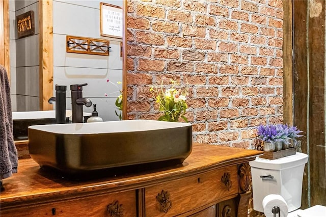 bathroom featuring vanity, toilet, and brick wall