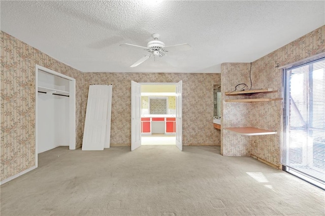 unfurnished bedroom featuring carpet floors, ceiling fan, a textured ceiling, and wallpapered walls