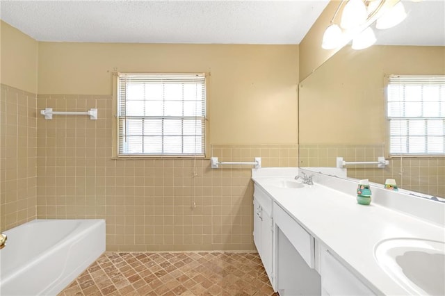 full bath featuring a healthy amount of sunlight, a textured ceiling, tile walls, and a sink