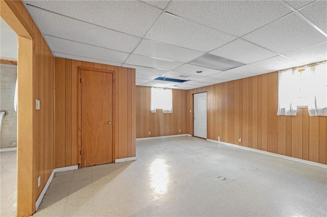 basement with a drop ceiling, wood walls, baseboards, and tile patterned floors