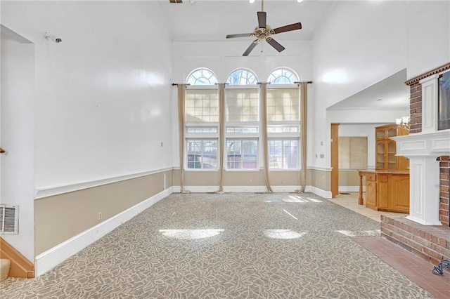 unfurnished living room featuring a towering ceiling, visible vents, baseboards, and a ceiling fan