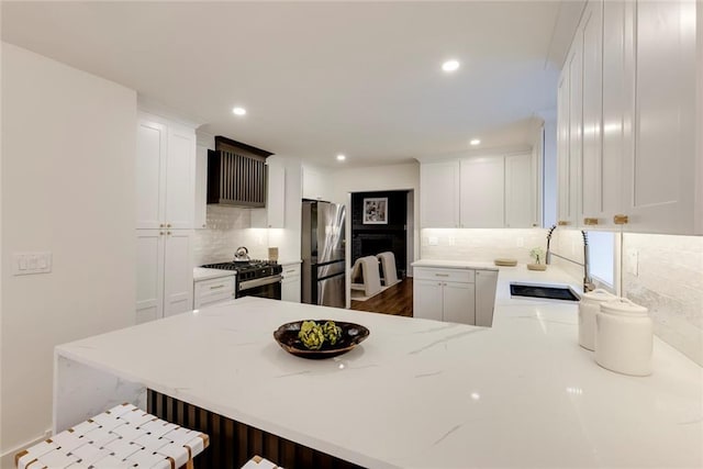 kitchen featuring sink, a breakfast bar area, stainless steel refrigerator, gas stove, and kitchen peninsula