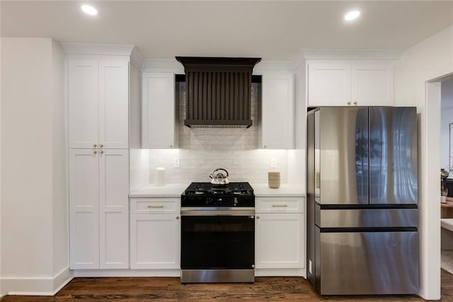 kitchen featuring stainless steel refrigerator, white cabinetry, gas stove, and wall chimney range hood