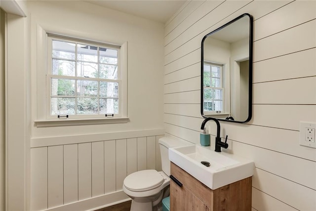 bathroom featuring vanity, a wealth of natural light, wood walls, and toilet