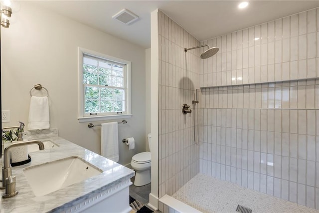 bathroom featuring vanity, a tile shower, and toilet