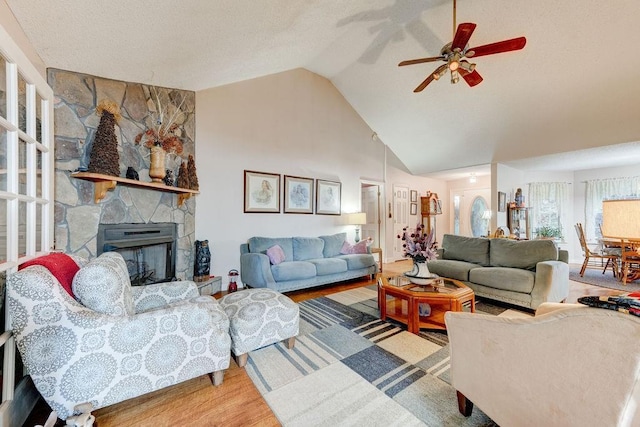 living room with ceiling fan, high vaulted ceiling, wood-type flooring, and a stone fireplace