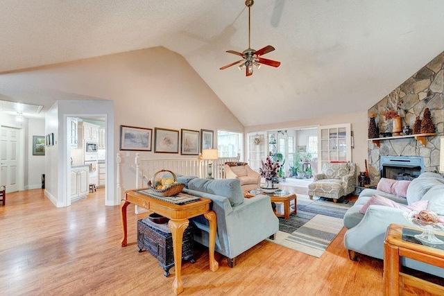 living room featuring light hardwood / wood-style floors, high vaulted ceiling, ceiling fan, and a fireplace