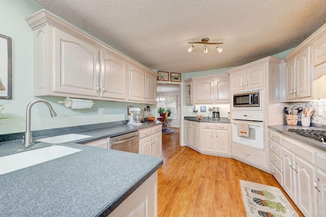 kitchen with appliances with stainless steel finishes, sink, backsplash, a textured ceiling, and light hardwood / wood-style floors