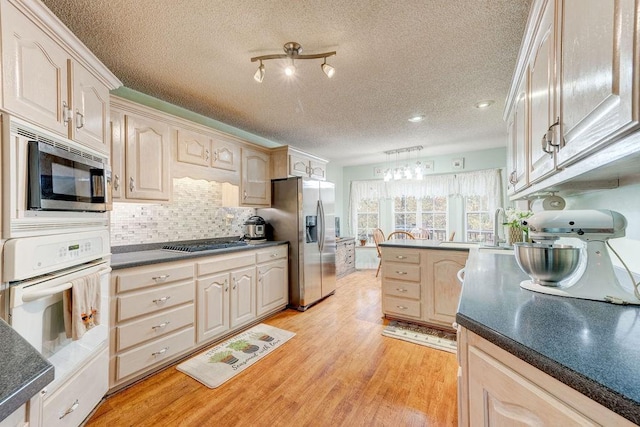 kitchen featuring appliances with stainless steel finishes, light hardwood / wood-style flooring, tasteful backsplash, light brown cabinetry, and a textured ceiling