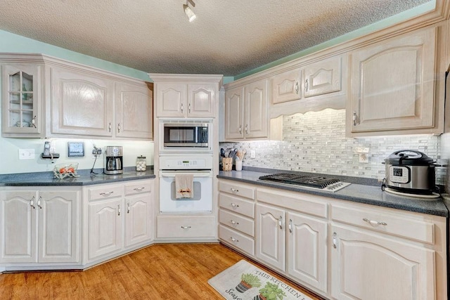 kitchen featuring a textured ceiling, tasteful backsplash, stainless steel appliances, and light hardwood / wood-style flooring