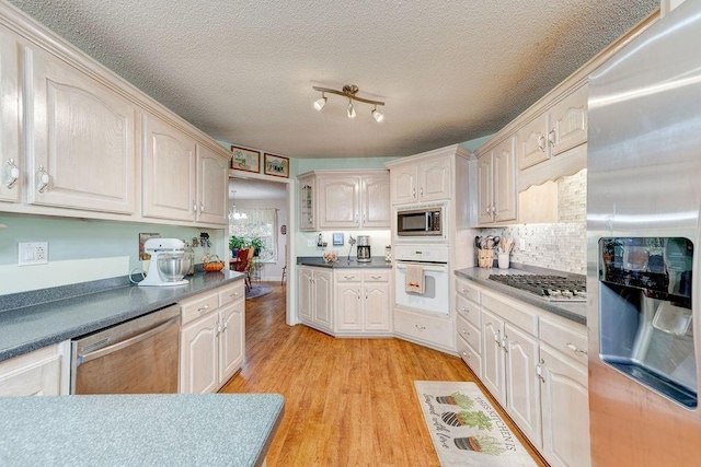 kitchen with a textured ceiling, appliances with stainless steel finishes, decorative backsplash, and light hardwood / wood-style flooring