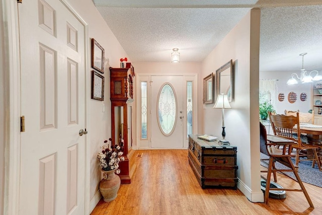 entryway featuring light wood-type flooring, a textured ceiling, and a notable chandelier