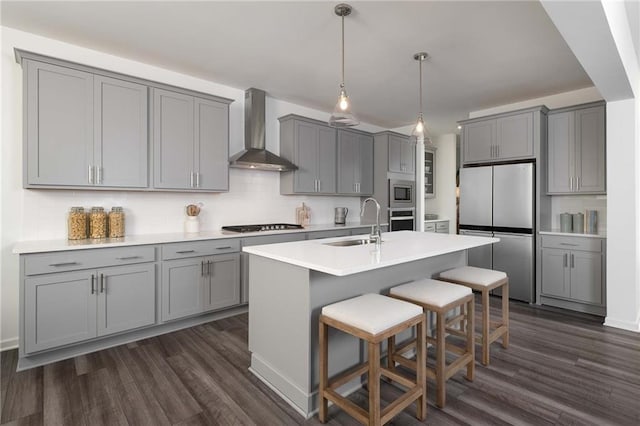 kitchen featuring pendant lighting, sink, wall chimney exhaust hood, gray cabinets, and stainless steel appliances