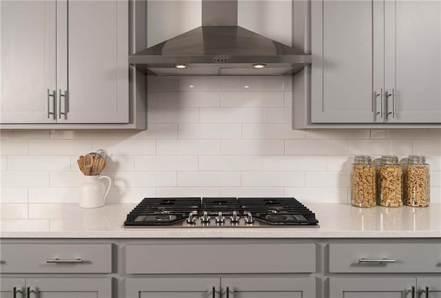 kitchen with decorative backsplash, stainless steel gas cooktop, wall chimney exhaust hood, and gray cabinetry