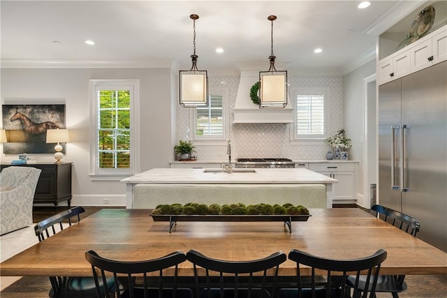 kitchen with crown molding, stainless steel built in fridge, a sink, light countertops, and a kitchen island with sink