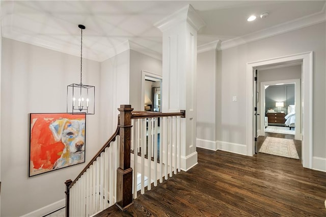 hall with an upstairs landing, dark wood-type flooring, ornamental molding, a chandelier, and baseboards