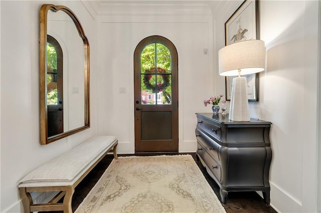 entryway featuring arched walkways, baseboards, and crown molding