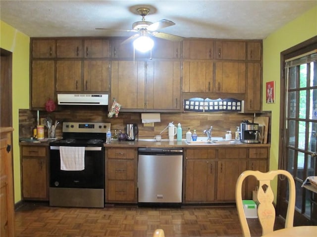 kitchen featuring stainless steel appliances, ventilation hood, a sink, a ceiling fan, and brown cabinetry