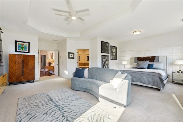 carpeted bedroom featuring a tray ceiling, connected bathroom, and ceiling fan