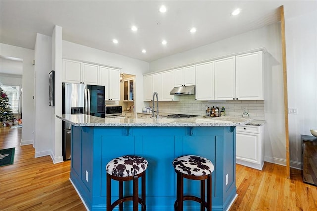 kitchen with white cabinetry, light stone counters, a breakfast bar, a center island with sink, and light wood-type flooring