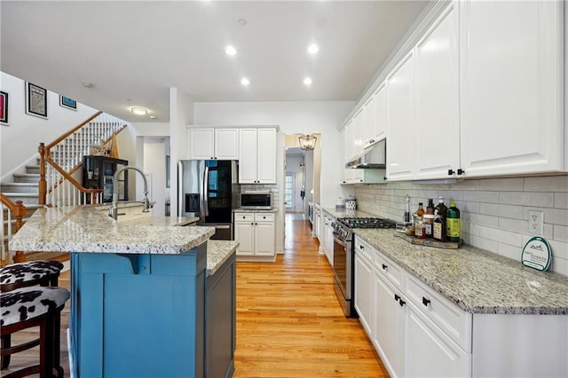 kitchen featuring a kitchen island with sink, white cabinets, light hardwood / wood-style floors, a kitchen bar, and stainless steel appliances